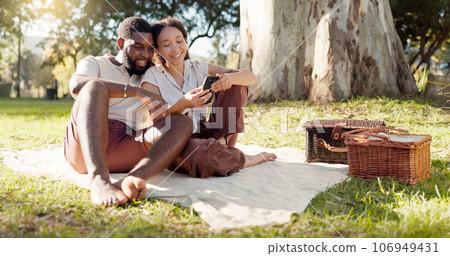 Happy, social media and an interracial couple on a picnic with a phone for communication, tech or an app. Talking, summer and a black man and woman with a mobile for a chat on a date in a park 106949431
