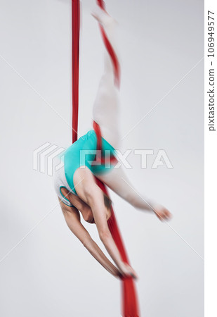 Sport, acrobat and aerial silk with a woman in air for performance, gymnastics and balance. Young athlete person or gymnast hanging on red fabric and white background with space, art and creativity Sport, acrobat and aerial silk with a woman in air for performance, gymnastics and balance. Young athlete person or gymnast hanging on red fabric and white background with space, art and creativity 106949577