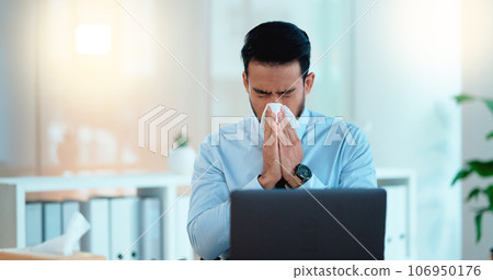 A modern business man feeling sick with covid fatigue while working online at a desk on his laptop. Closeup of an male corporate manager blowing his nose. An ill office worker frustrated at work. A modern business man feeling sick with covid fatigue while working online at a desk on his laptop. Closeup of an male corporate manager blowing his nose. An ill office worker frustrated at work. 106950176