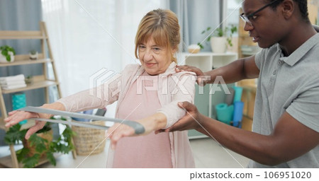 Physiotherapy, arms resistance band and old woman for rehabilitation, recovery or help for motion training. Physical therapy, black man or physiotherapist stretching senior woman for mobility problem 106951020