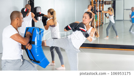 Hispanic woman kicking boxing shield during self-defense course Hispanic woman kicking boxing shield during self-defense course 106953175