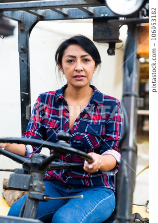 Confident hispanic woman sits behind the wheel of a forklift truck. 106953182
