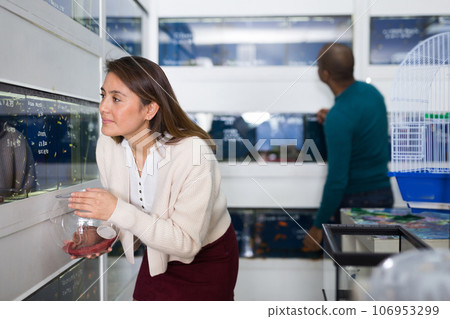 Portrait of interested young woman looking at colorful tropical fish in aquariums in shop 106953299