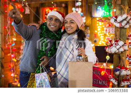 Married couple point finger at selected christmas tree decorations at street market Married couple point finger at selected christmas tree decorations at street market 106953388
