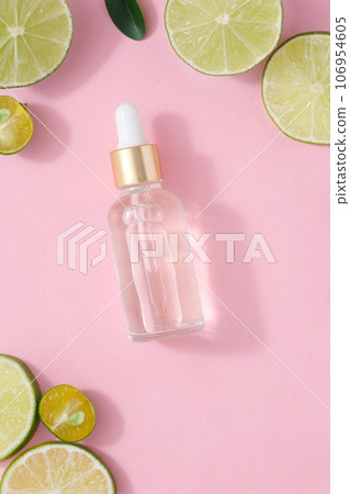 A glass dropper bottle without label decorated with slices of lime and kumquat on a pink background. Mockup scene for advertising with natural extract and natural essential 106954605
