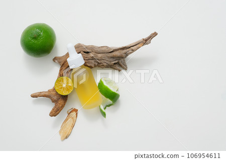 A yellow dropper bottle unbranded displayed on white background with kumquat slices and halves of lime decorated with green leaves and dry twig. Blank space for display product 106954611