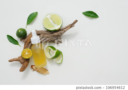 Natural vitamin C skincare product with fresh lime slices decorated with green leaves and dry twig on white background. Minimalist concept for advertising. Copy space 106954612