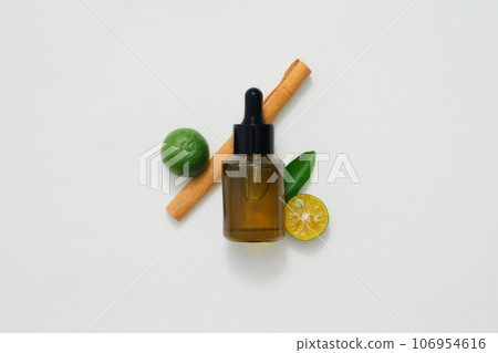 An amber dropper bottle decorated with ingredients for natural essential oils on a white background. Lemon, kumquat and cinnamon are all essential oils with pleasant scents 106954616