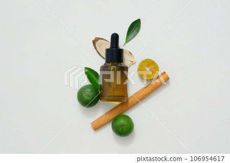 Scene for advertising essential oil products or scent solutions. Dropper bottle containing essential oils decorated with lemon, kumquat and cinnamon on a white background. 106954617