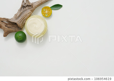 Top view of yellow jar filled with cream texture, decorated with slices of kumquat, dry twig and green leaves on a white background. Empty space for mockup bottle display 106954619