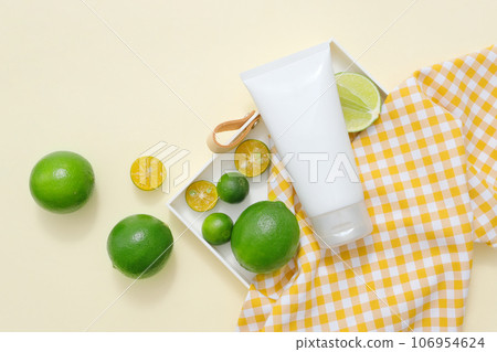 A white plastic tube container moisturizer cream or facial cleanser with ingredient from natural extract, decorated with lime and kumquat slices on beige background 106954624