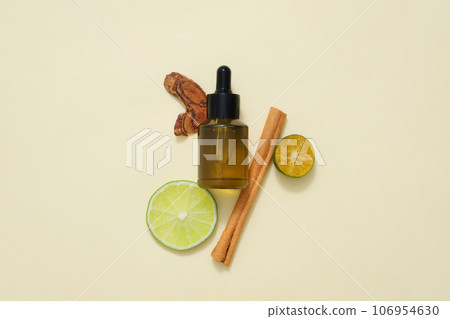 An amber bottle decorated with kumquat and lime slices and cinnamon stick on beige background. Natural ingredients containing aromatic essential oils for scent solutions 106954630