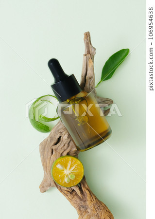 Concept of natural cosmetics with lime extract. A dropper bottle unbranded displayed on dry twig with kumquat slice and leaf. Top view, minimalist concept 106954638