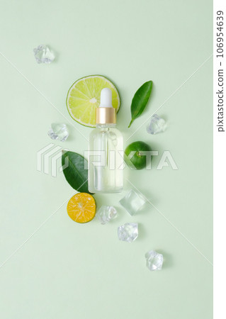 Template cosmetic mockup with glass dropper bottle decorated with kumquat, lime, green leaves and ices on pastel background. Cosmetics concept with natural extract rich in vitamin C 106954639