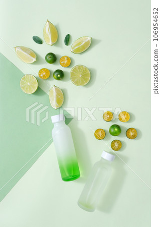 Scene for advertising product with ingredient from natural essential from lime and kumquat. Slices of lime and kumquat decorated with empty bottles on pastel background 106954652