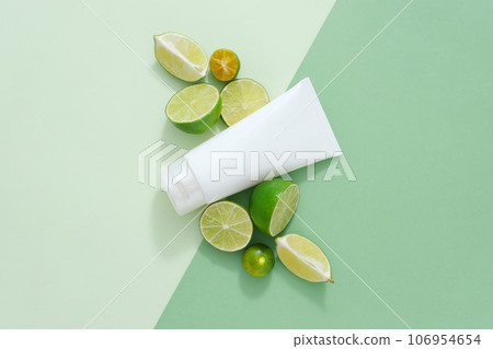 Top view, flat lay of white plastic tube decorated with fresh slices of lime and kumquat on paper background. Minimalist concept for advertising product with natural extract 106954654