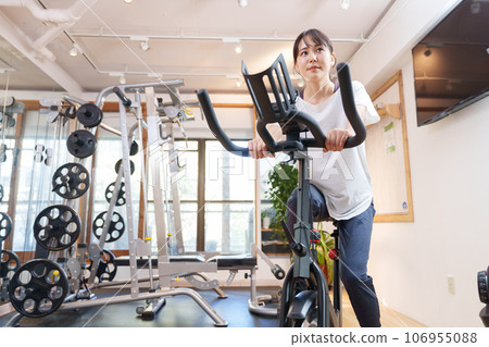 A woman exercising on an exercise bike at a sports gym (health/diet) A woman exercising on an exercise bike at a sports gym (health/diet) 106955088