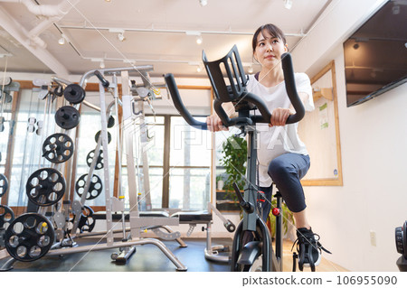 A woman exercising on an exercise bike at a sports gym (health/diet) A woman exercising on an exercise bike at a sports gym (health/diet) 106955090