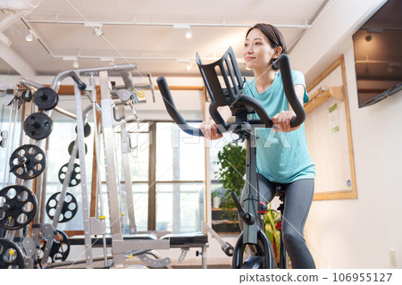 A woman exercising on an exercise bike at a sports gym (health/diet) A woman exercising on an exercise bike at a sports gym (health/diet) 106955127