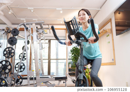 A woman exercising on an exercise bike at a sports gym (health/diet) A woman exercising on an exercise bike at a sports gym (health/diet) 106955128