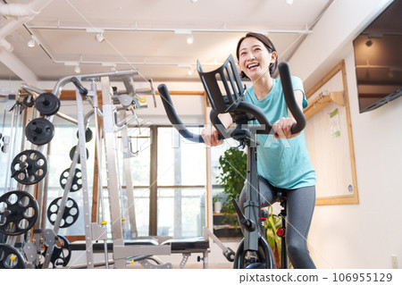 A woman exercising on an exercise bike at a sports gym (health/diet) 106955129