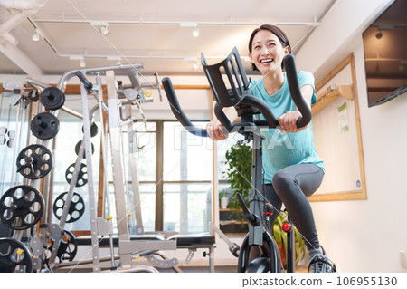 A woman exercising on an exercise bike at a sports gym (health/diet) 106955130