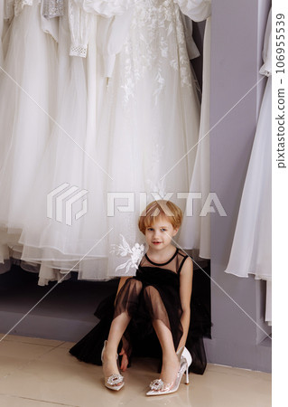 Little girl in a black evening dress in a clothing boutique Little girl in a black evening dress in a clothing boutique 106955539