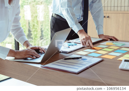 Business colleagues putting sticky notes and typing data on laptop to coworking about new business Business colleagues putting sticky notes and typing data on laptop to coworking about new business 106956134