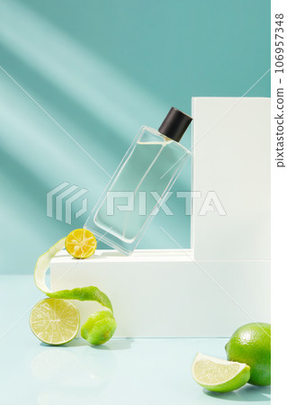 Transparent spray bottle is leaning on the white podium, decorated with kumquats and limes. Essential oil extracted from Lime and Kumquat can be used in perfume production 106957348