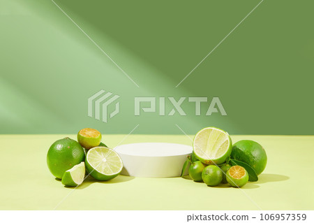 Against the green background, a podium in white color is displayed with piles of kumquats and limes. 106957359