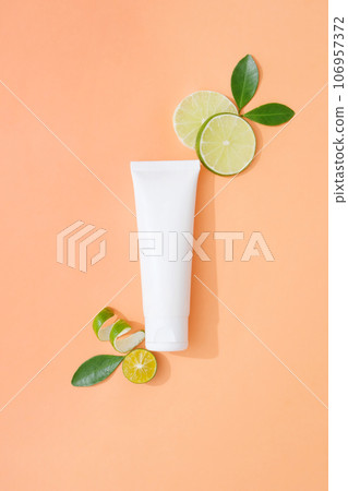 Minimal scene of empty label white tube decorated on coral background with slices of kumquat and lime. Lime and Kumquat can pack a nutritional punch for your diet 106957372