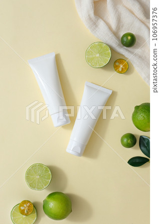 Over the beige background, two unbranded tubes are displayed with some fresh lime and kumquat slices. Lime and Kumquat juice is enriched with Vitamin C 106957376