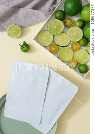 Facial mask sheet without label placed on a ceramic dish. A tray containing kumquat and lime slices displayed with a towel. Mockup template for branding 106957377