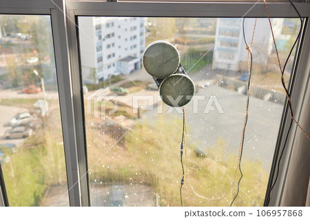 A window cleaner robot washes glass against the backdrop of multi-storey buildings. 106957868