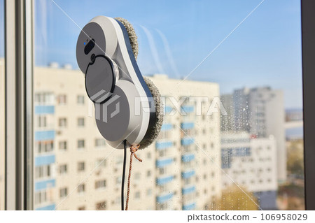 A window cleaner robot washes glass against the backdrop of multi-storey buildings. 106958029