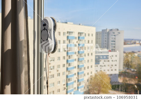 A window cleaner robot washes glass against the backdrop of multi-storey buildings. 106958031