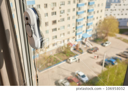 A window cleaner robot washes glass against the backdrop of multi-storey buildings. 106958032