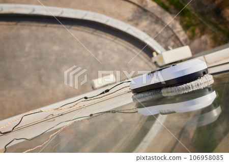 A window cleaner robot washes glass against the backdrop of multi-storey buildings. 106958085