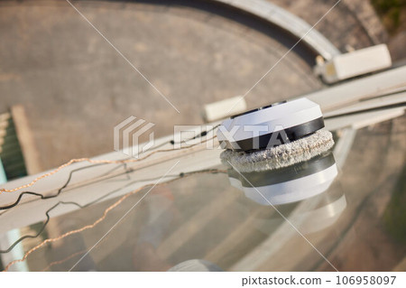 A window cleaner robot washes glass against the backdrop of multi-storey buildings. A window cleaner robot washes glass against the backdrop of multi-storey buildings. 106958097