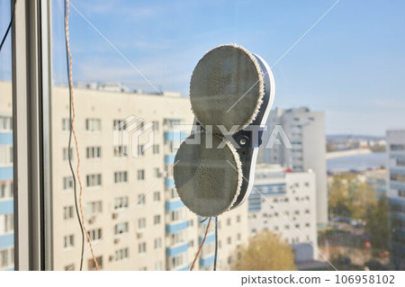 A window cleaner robot washes glass against the backdrop of multi-storey buildings. 106958102