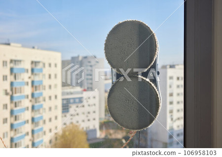 A window cleaner robot washes glass against the backdrop of multi-storey buildings. 106958103