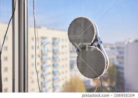 A window cleaner robot washes glass against the backdrop of multi-storey buildings. 106958104