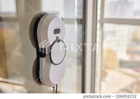 A window cleaner robot washes glass against the backdrop of multi-storey buildings. 106958152