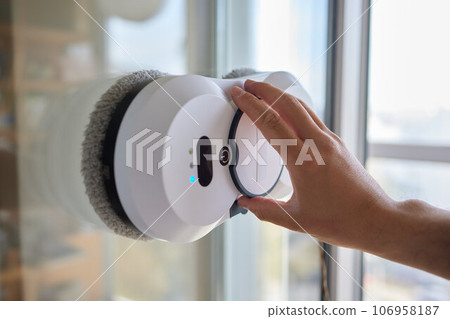 A window cleaner robot washes glass against the backdrop of multi-storey buildings. 106958187