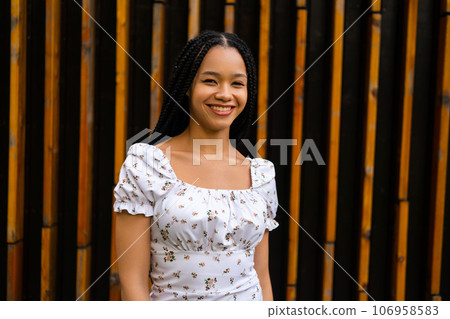 Portrait of a young pretty afro woman with pigtails who smiles beautifully and looks at the camera in a white dress with flowers Portrait of a young pretty afro woman with pigtails who smiles beautifully and looks at the camera in a white dress with flowers 106958583