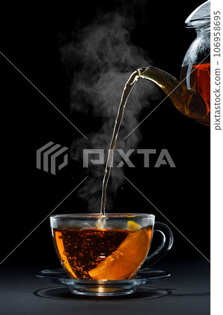 hot black tea pouring from teapot into glass cup with lemon hot black tea pouring from teapot into glass cup with lemon 106958695