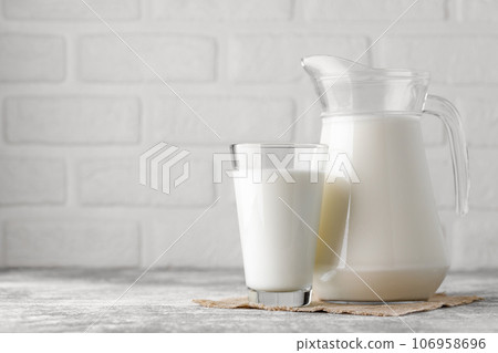 milk in jug and glass on table with white brick wall as background milk in jug and glass on table with white brick wall as background 106958696
