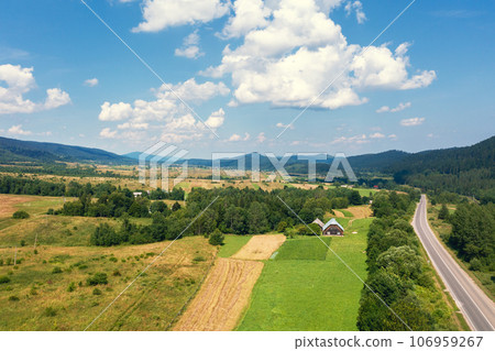 Aerial view of a mountain valley. Rural landscape in summer. View of the village, highway, and mountains on a sunny day Aerial view of a mountain valley. Rural landscape in summer. View of the village, highway, and mountains on a sunny day 106959267