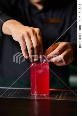 Barman in shirt and apron making an alcoholic drink with ice in a cocktail glass. 106959383