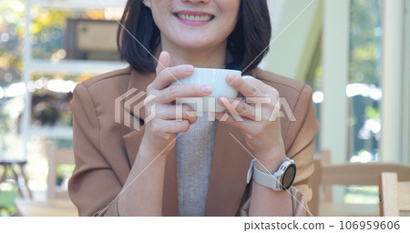 Woman holding coffee cup relaxing after work at office warm taste in cafe. Close up hands of woman sitting office desk holding sweet coffee cup relax and enjoy with happy time. Hot coffee mug in hand 106959606